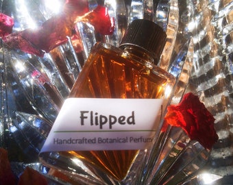 May include: A small amber glass bottle with a black cap, filled with a golden liquid. The bottle is labeled "Flipped Handcrafted Botanical Perfume".