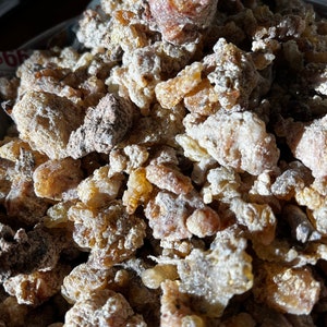 May include: A close-up of a pile of light brown and amber resin pieces. The resin is irregularly shaped and has a slightly powdery texture.