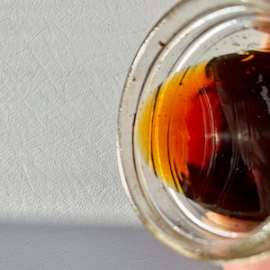 May include: A clear glass jar with a brown liquid inside. The liquid is thick and has a dark brown color.