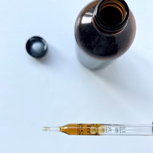May include: A brown glass bottle with a black cap and a dropper filled with a clear liquid. The dropper has markings for 1 ml and 2 ml.