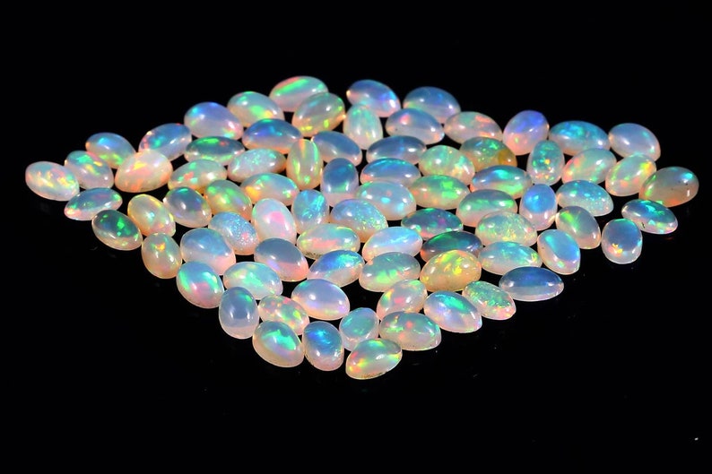 Puede incluir: Una colecci&oacute;n de piedras preciosas de &oacute;palo de forma ovalada e iridiscente. Los &oacute;palos son de color blanco p&aacute;lido con destellos de azul, verde y amarillo.