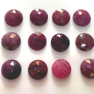 May include: Twelve round, faceted ruby gemstones arranged in a three-by-four grid. Each stone features a deep magenta to dark red hue with a polished, multi-faceted surface that reflects light, creating a sparkling, geometric pattern across the top.