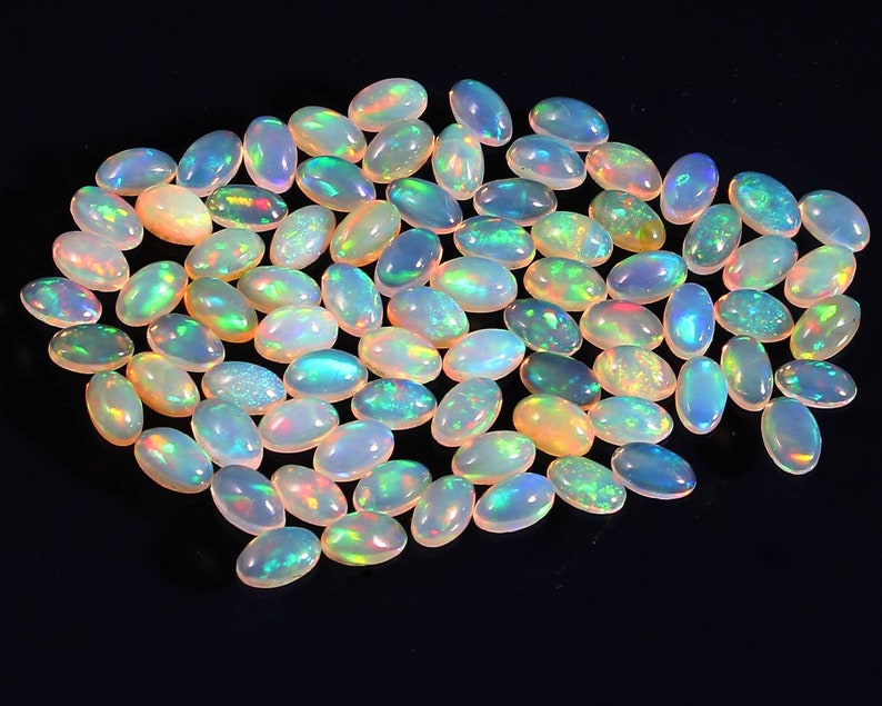 Puede incluir: Una colecci&oacute;n de piedras preciosas de &oacute;palo de forma ovalada e iridiscentes. Los &oacute;palos son de color blanco p&aacute;lido con destellos de azul, verde y amarillo.