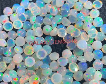 Op de afbeelding: Een verzameling gepolijste opaal edelstenen, met een scala aan kleuren, waaronder wit, blauw, groen en rood. De opalen zijn rond en cabochon geslepen, met een zichtbaar kleurenspel effect. De tekst "GALAXY GEMS2018" is zichtbaar.