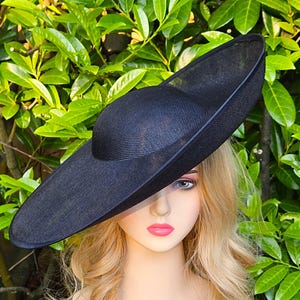 May include: A large, black, wide-brimmed hat made of a woven material. The hat has a rounded crown and a wide, flat brim that curves up slightly at the edges.