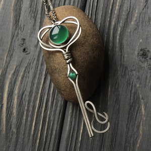 May include: A silver key pendant necklace with green gemstone accents. The key is intricately designed with a heart-shaped loop at the top and a decorative swirl at the bottom.