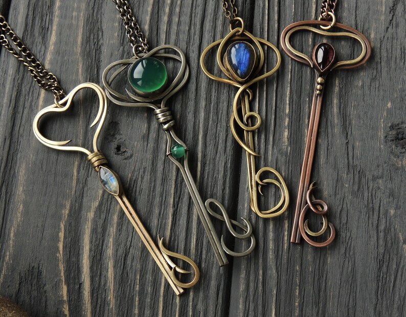 May include: Four ornate key-shaped necklaces with different colored gemstones. The necklaces are made of silver and brass and feature intricate designs.