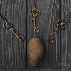 May include: Three ornate key-shaped pendants with green and blue gemstones hanging from chains on a dark wood background. The pendants are made of wire and have intricate designs. The text "Yasmirh jewelry custom & fancy" is visible in the bottom right corner of the image.