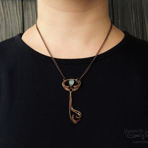 May include: A copper necklace with a key-shaped pendant featuring a green gemstone. The pendant has intricate details and a delicate chain.