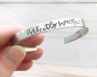 May include: Silver bracelet with the words "Perfectly Imperfect" engraved on it.