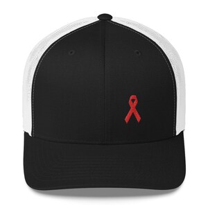 May include: A black and white trucker hat with a red ribbon embroidered on the front. The hat has a mesh back.