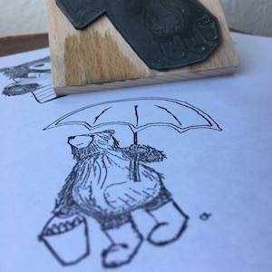 May include: A black and white illustration of a bear holding an umbrella. The bear is wearing a hooded jacket and boots. The bear is walking in the rain.