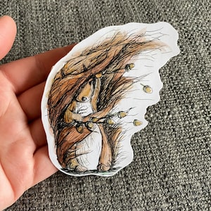 Könnte beinhalten: Eine Aquarell-Illustration eines braunen Eichhörnchens, das Eicheln in seinen Pfoten hält, umgeben von fallenden Eicheln. Das Eichhörnchen ist mit einem buschigen Schwanz und einem verspielten Ausdruck dargestellt.