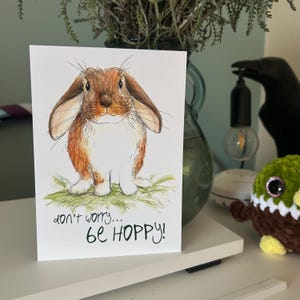 BE HOPPY BUNNY cartolina Catherine Redgate lettera carta positività felice carino stampa accogliente arte illustrazione coniglio gioco di parole positivo animale animale domestico peloso
