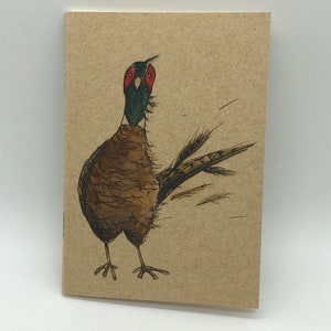May include: A brown and white pheasant with a red and green head is drawn on a brown paper card.
