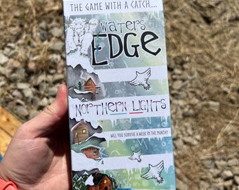 May include: A rectangular board game box titled "Waters Edge Northern Lights." The box features illustrations of cabins, birds, and a snowy landscape. The text "The Game With A Catch" and "Will You Survive a Week in the North?" are also visible.