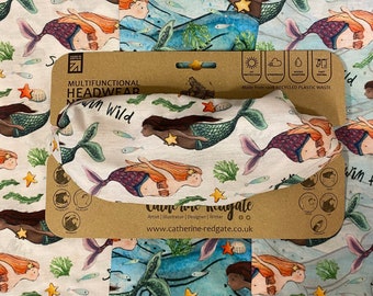 May include: A white and blue patterned headwear with mermaids, seaweed, and stars. The headwear is made from recycled plastic waste. The text "MULTIFUNCTIONAL HEADWEAR swim Wild" is printed on the packaging. The text "Catherine Redgate Artist Illustrator | Designer | Writer www.catherine-redgate.co.uk" is also printed on the packaging.