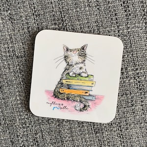 May include: Square coaster featuring a watercolor illustration of a gray and white cat sitting on a stack of books. The text "anything is possible" is written in a cursive font at the bottom of the coaster.