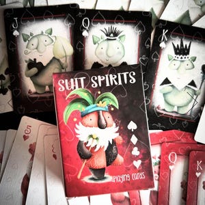 May include: A deck of playing cards with a red box featuring the text "Suit Spirits Playing Cards". The box shows a cartoon character with a red and white suit, a green hat, and a white beard. The cards feature illustrations of cartoon characters with different suits.
