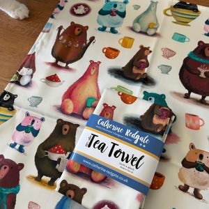 Può includere: Un canovaccio bianco con un motivo ripetuto di orsi dei cartoni animati e tazze da tè. Il canovaccio è confezionato con un'etichetta che recita "Tea Towel" e "Catherine Redgate". Il canovaccio misura 72 cm x 46 cm.