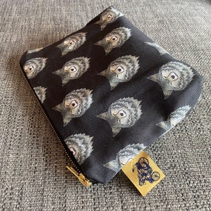 Puede incluir: Bolsa de lona negra con cremallera con un patr&oacute;n repetido de caras de lobos grises. La bolsa tiene una cremallera dorada y una peque&ntilde;a etiqueta de cuero marr&oacute;n con un dise&ntilde;o de bicicleta.