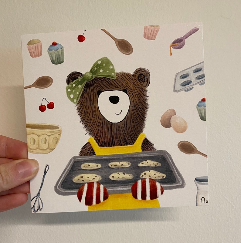 Puede incluir: Un oso marr&oacute;n con un delantal amarillo y un lazo verde sostiene una bandeja para hornear con galletas. La bandeja para hornear tiene 6 galletas. El oso est&aacute; rodeado de ilustraciones con tem&aacute;tica de horneado, que incluyen cupcakes, cerezas y un rodillo.