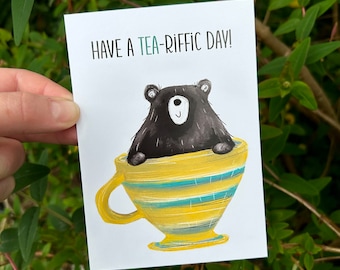May include: A greeting card with a black bear sitting in a yellow and blue striped teacup. The card reads "Have a tea-riffic day!"