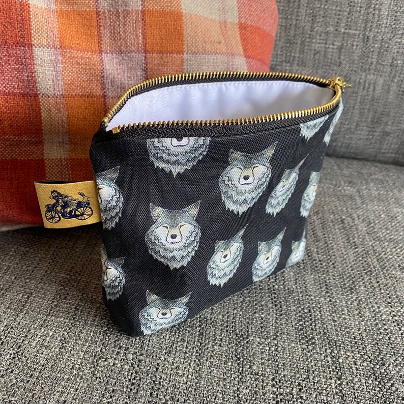 Puede incluir: Bolsa negra con cremallera y forro blanco. La bolsa est&aacute; cubierta con un patr&oacute;n repetido de caras de lobo.