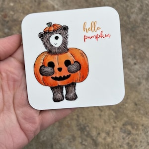 May include: A brown bear wearing a pumpkin costume with the text "hello pumpkin" on a white background.