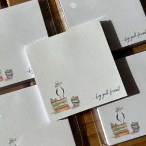 Può includere: Un set di biglietti da visita vuoti con un'illustrazione ad acquerello di un gabbiano in piedi su una pila di libri con il testo "...hey gull friend!" su ogni biglietto.
