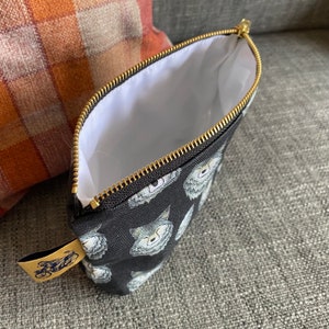 Puede incluir: Bolsa negra con cremallera, forro blanco y un patr&oacute;n repetido de caras de lobo. La bolsa tiene una cremallera dorada y una etiqueta dorada con un dise&ntilde;o de bicicleta.