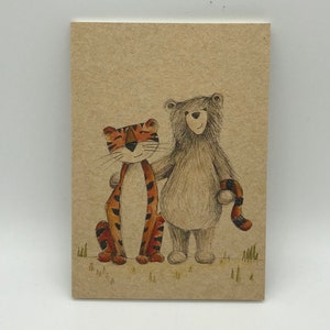 May include: A greetings card with a charming illustration of a tiger and a bear. The tiger is orange with black stripes, and the bear is brown. They are standing together on a grassy area, with a light brown background.