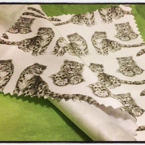 May include: White fabric with a repeating pattern of black and white snow leopards. The fabric is folded in half, showing the back side of the fabric.