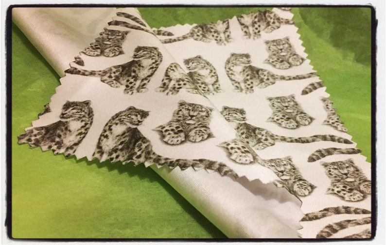 May include: White fabric with a repeating pattern of black and white snow leopards. The fabric is folded in half, showing the back side of the fabric.
