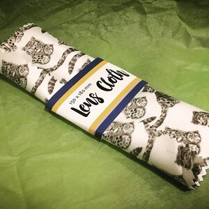 May include: A white lens cleaning cloth with a black and white leopard print. The cloth is rolled up and has a label that says "Lens Cloth" and "150 x 180 mm".