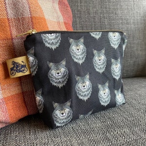 Puede incluir: Bolsa de cremallera de lona negra con un patr&oacute;n repetido de caras de lobo grises.