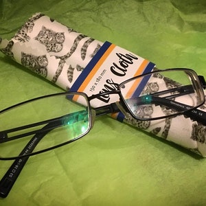 May include: Black rectangular reading glasses with a white and gray patterned lens cloth. The cloth has the text "Lens Cloth" and "150 x 180 mm" printed on it.