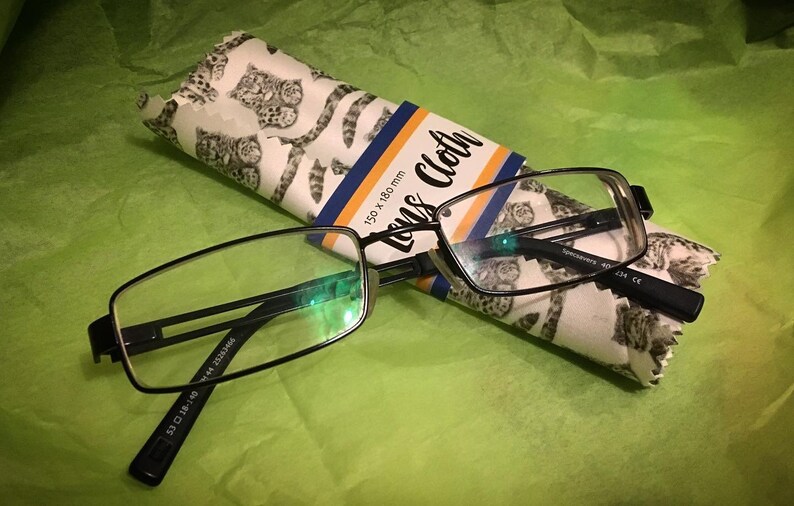 May include: Black rectangular reading glasses with a white and gray patterned lens cloth. The cloth has the text "Lens Cloth" and "150 x 180 mm" printed on it.