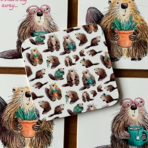 May include: Square white coaster with a repeating pattern of cartoon beavers. The beavers are brown and wearing glasses, holding mugs, or carrying plants in pots. The coaster is surrounded by other coasters with similar beaver illustrations.