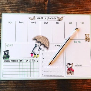 Könnte beinhalten: Ein Wochenplaner mit grünem und weißem Design mit Illustrationen von Bären und Eichhörnchen. Der Planer enthält Abschnitte für Ziele, Mahlzeiten und To-Do-Listen sowie einen Wochen-Tracker.