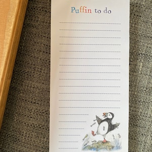 Könnte beinhalten: Eine weiße To-Do-Liste mit den Worten "Puffin to do" in bunten Buchstaben oben. Eine Cartoon-Illustration eines Papageientauchers, der einen Fisch im Schnabel hält, befindet sich unten auf der Liste.