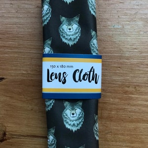 May include: A black microfiber lens cleaning cloth with a repeating pattern of wolf faces. The cloth is folded in half and has a label that reads "Lens Cloth" and "150 x 180 mm".