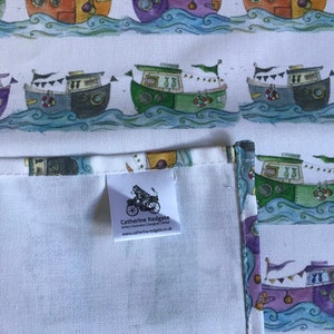 Peut inclure: Une serviette de cuisine blanche avec un motif coloré de bateaux sur une mer bleue. La serviette de cuisine porte une étiquette qui dit "Catherine Redgate, Artiste | Illustratrice | Designer | Vendeur, www.catherineredgate.co.uk".