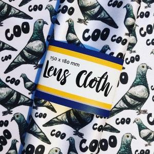 以下が含まれることがあります： 白地に黒と白の鳩と「COO」の文字が繰り返しプリントされたレンズクロス。クロスには「Lens Cloth」と「150 x 180 mm」と書かれた青と黄色のラベルが付いています。