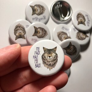 Op de afbeelding: Een witte knop met een wolfillustratie en de tekst "My pack has my back".