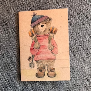 May include: A watercolor illustration of a brown bear wearing a purple hat and a pink sweater. The bear is carrying a backpack with two brown cylinders on the sides. The bear is standing on a brown background.