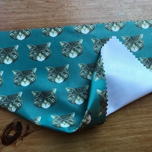 May include: A teal blue microfiber cleaning cloth with a repeating pattern of tabby cat faces. The cloth is folded in half, revealing a white microfiber side.