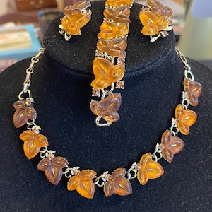 May include: A vintage amber glass leaf necklace, bracelet, and earrings set. The jewelry features carved leaves with rhinestones accents.