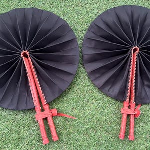 May include: Two black folding fans with red handles. The fans are closed and have a traditional design.