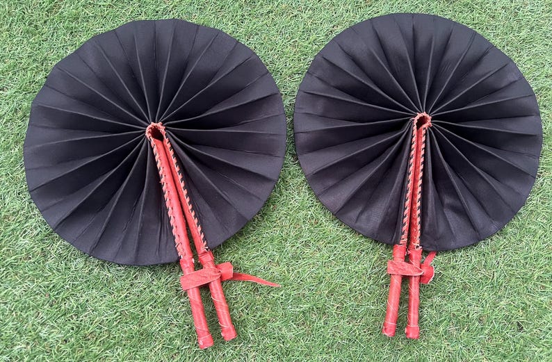 May include: Two black folding fans with red handles. The fans are closed and have a traditional design.